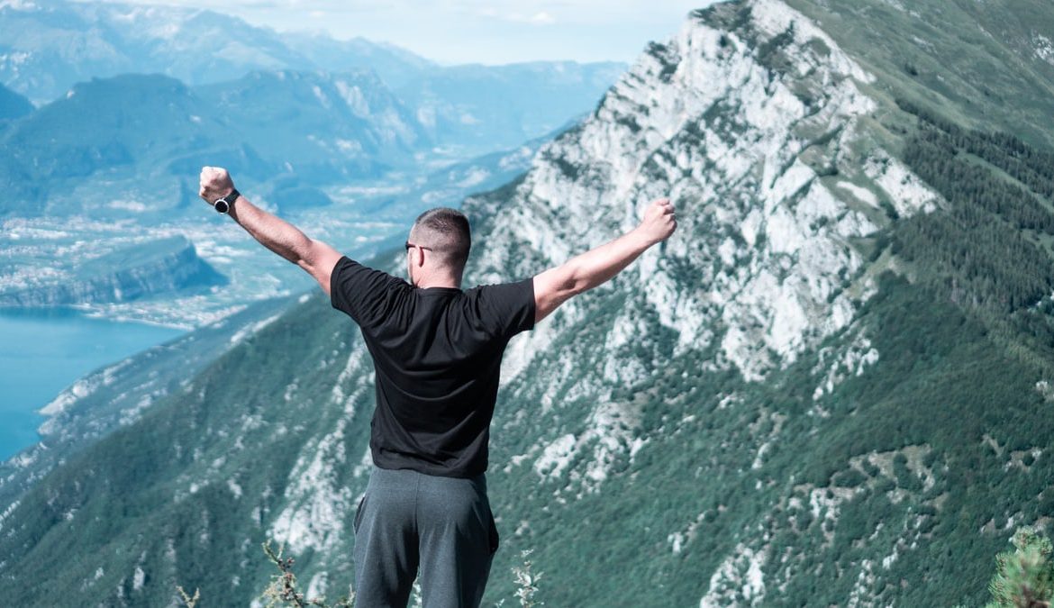 Man standing with arms raised in celebration overlooking a breathtaking mountain landscape.