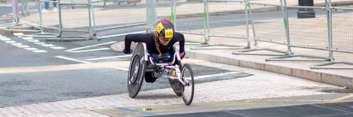 A dedicated athlete competes in a marathon using a racing wheelchair on city streets.